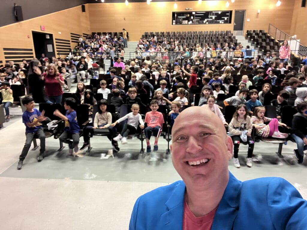 Smiling man with children in auditorium.